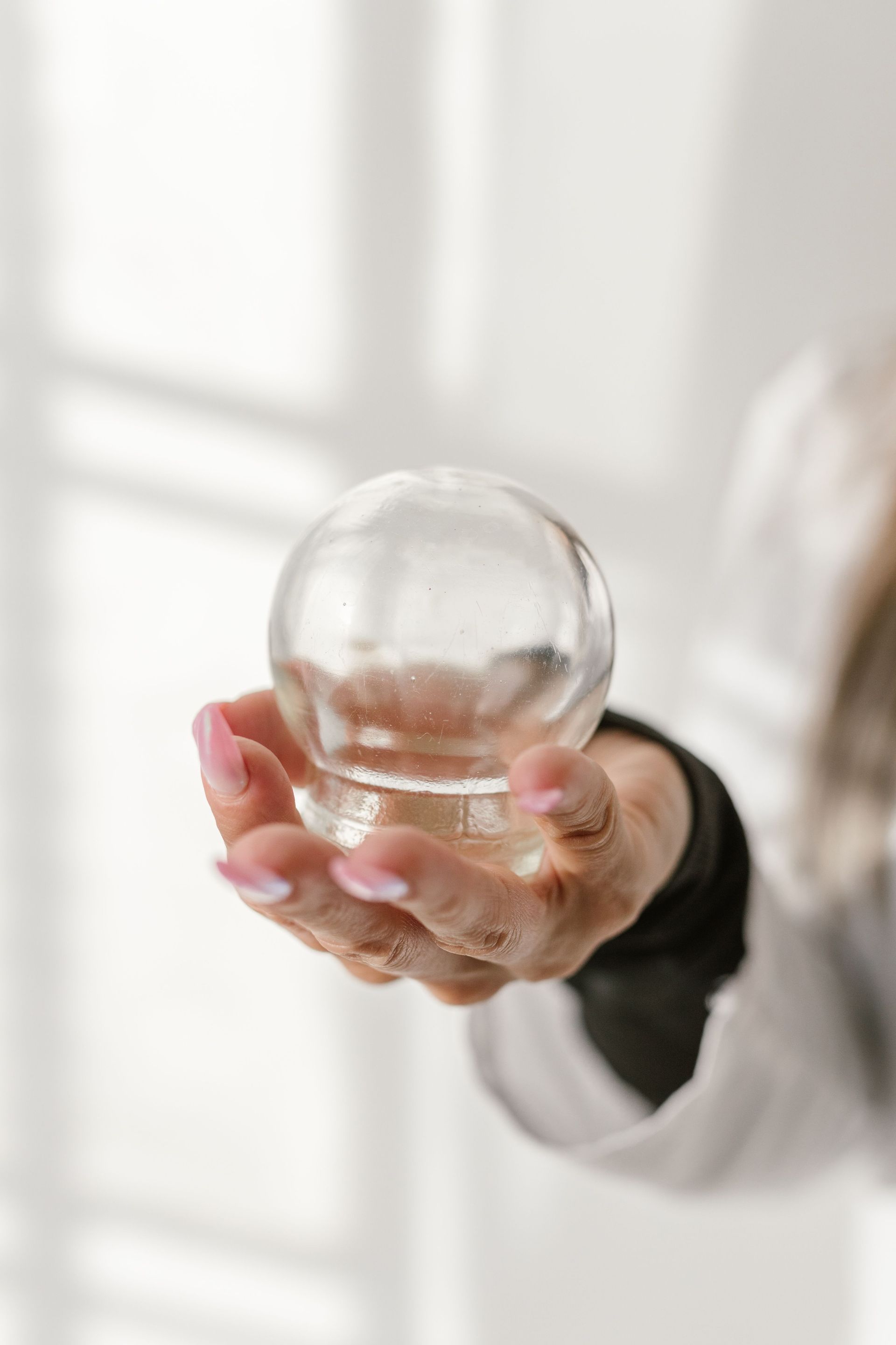 Close-up of a hand gracefully holding a glass sphere against a light background.